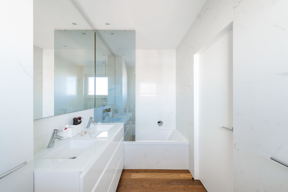 Design ideas for a mid-sized contemporary master bathroom in Milan with flat-panel cabinets, white cabinets, an alcove tub, white tile, stone slab, white walls, medium hardwood floors, an integrated sink, solid surface benchtops and an open shower.