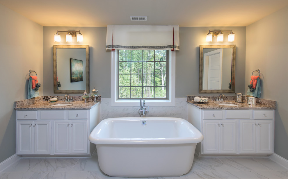 Design ideas for a large transitional master bathroom in Raleigh with recessed-panel cabinets, white cabinets, a freestanding tub, grey walls, marble floors, an undermount sink and granite benchtops.