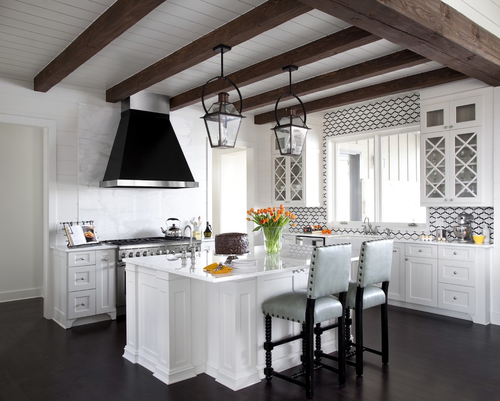 This is an example of a large transitional l-shaped open plan kitchen in New Orleans with a farmhouse sink, white cabinets, dark hardwood floors, with island, marble benchtops, white splashback, stone slab splashback, stainless steel appliances, white benchtop, exposed beam and shaker cabinets.