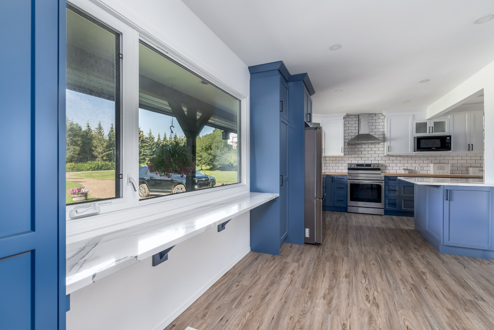 Example of a transitional kitchen design in Edmonton with shaker cabinets, blue cabinets, quartzite countertops, subway tile backsplash, stainless steel appliances, an island and white countertops