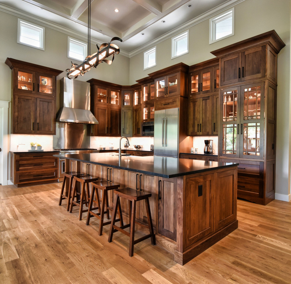 Inspiration for a traditional l-shaped eat-in kitchen in Other with a farmhouse sink, shaker cabinets, dark wood cabinets, granite benchtops, white splashback, stainless steel appliances, light hardwood floors, with island, brown floor, black benchtop, coffered and marble splashback.