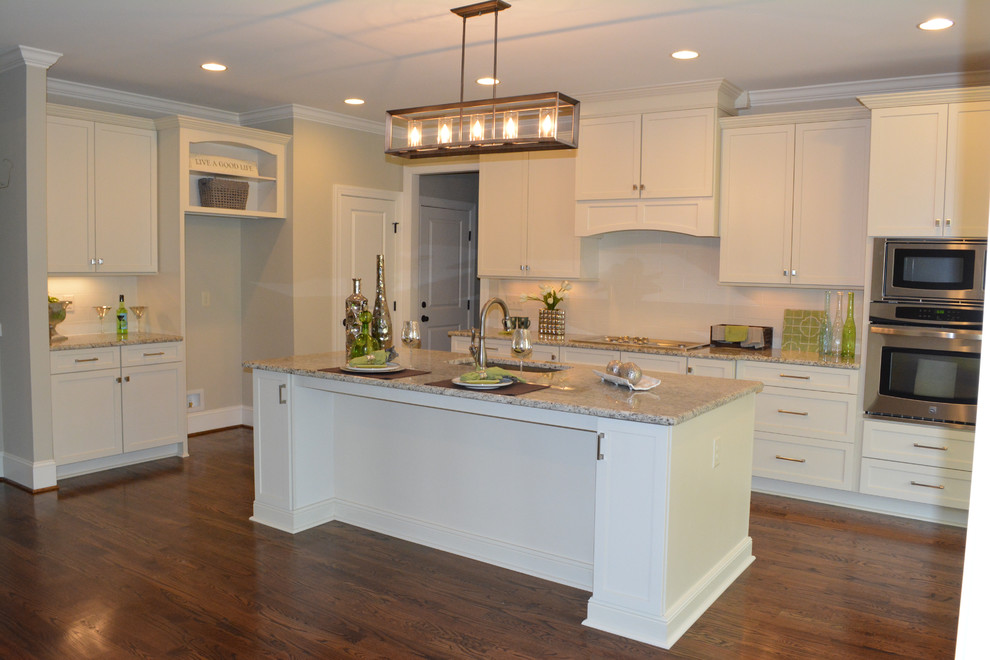 Photo of a mid-sized transitional l-shaped kitchen in Raleigh with an undermount sink, recessed-panel cabinets, white cabinets, granite benchtops, white splashback, ceramic splashback, stainless steel appliances, medium hardwood floors and with island.