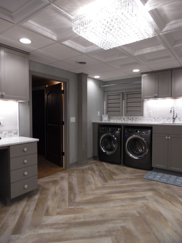 Inspiration for a large traditional utility room in Milwaukee with an undermount sink, recessed-panel cabinets, grey cabinets, quartz benchtops, vinyl floors, a side-by-side washer and dryer, brown floor and white benchtop.