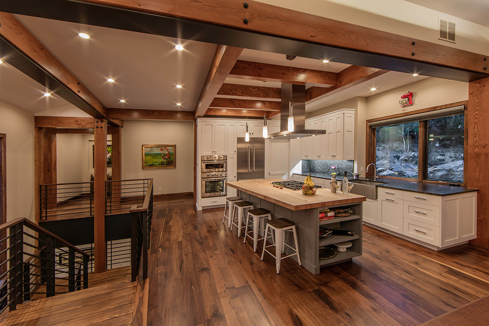 Design ideas for a large country l-shaped open plan kitchen in Denver with a farmhouse sink, shaker cabinets, wood benchtops, grey splashback, stone slab splashback, stainless steel appliances, dark hardwood floors, with island and white cabinets.