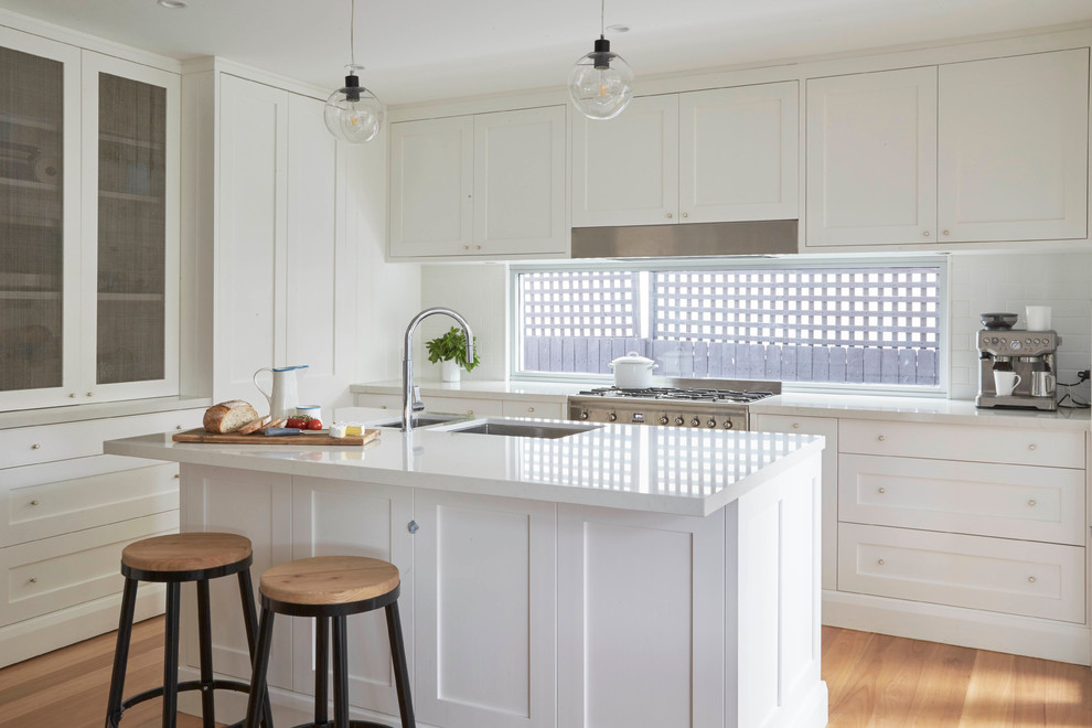 Mid-sized transitional l-shaped separate kitchen in Sydney with an undermount sink, shaker cabinets, white cabinets, white splashback, ceramic splashback, stainless steel appliances, medium hardwood floors and with island.
