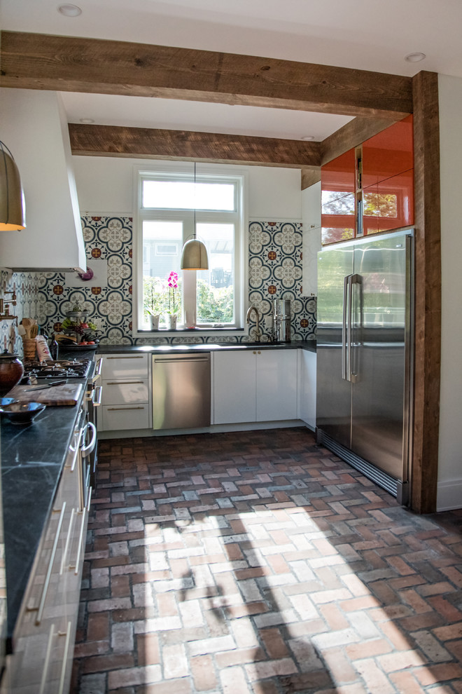 Design ideas for a mid-sized country u-shaped eat-in kitchen with an undermount sink, flat-panel cabinets, white cabinets, soapstone benchtops, multi-coloured splashback, cement tile splashback, stainless steel appliances, brick floors, no island and red floor.