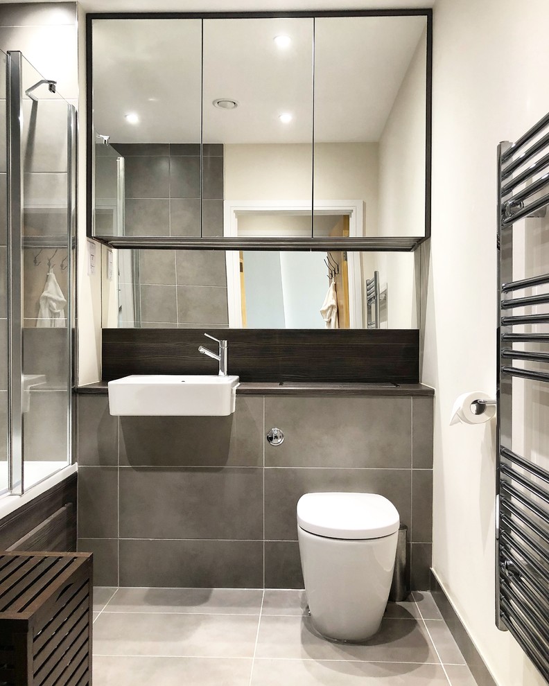 This is an example of a small modern master bathroom in London with glass-front cabinets, dark wood cabinets, a wall-mount toilet, ceramic floors, laminate benchtops and grey floor.