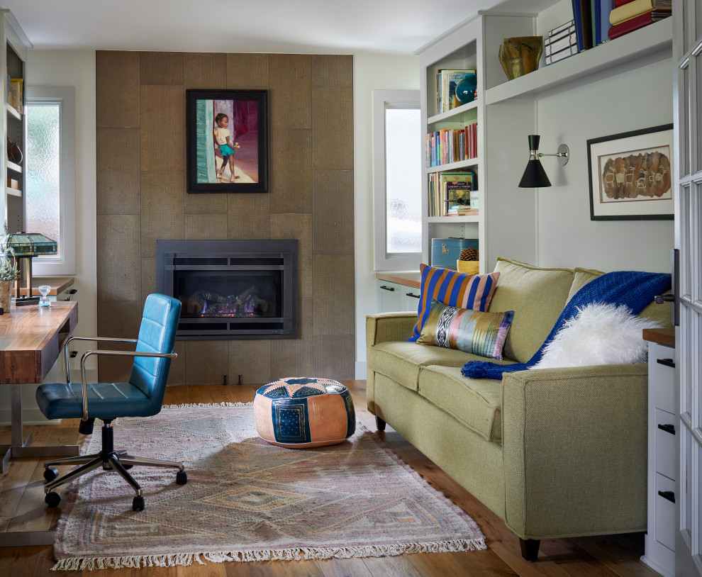 Photo of a midcentury home office in Denver with a library, white walls, light hardwood floors, a ribbon fireplace, a metal fireplace surround and a freestanding desk.