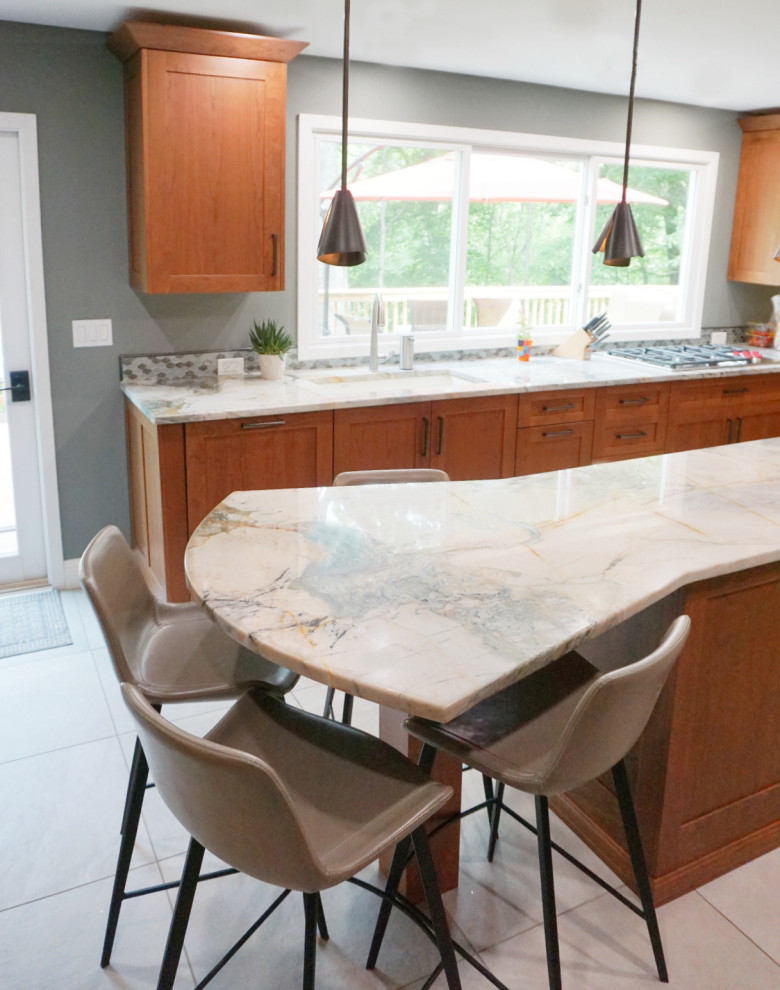 Mid-sized transitional porcelain tile and gray floor eat-in kitchen photo with recessed-panel cabinets, medium tone wood cabinets, quartzite countertops, green backsplash, mosaic tile backsplash, stainless steel appliances and an island