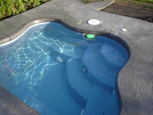 Backyard custom-shaped pool in Portland with a hot tub and concrete slab.