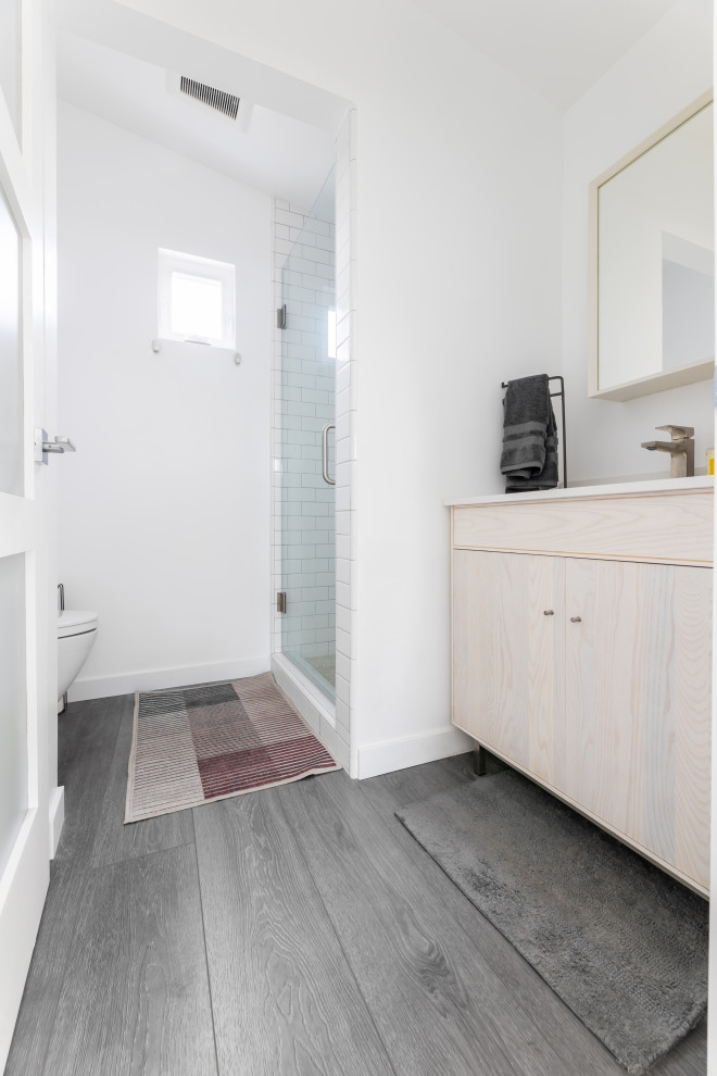 Exempel på ett litet modernt vit vitt badrum med dusch, med luckor med glaspanel, skåp i ljust trä, en dusch i en alkov, en toalettstol med hel cisternkåpa, vit kakel, keramikplattor, vita väggar, vinylgolv, ett nedsänkt handfat, marmorbänkskiva, grått golv och dusch med gångjärnsdörr