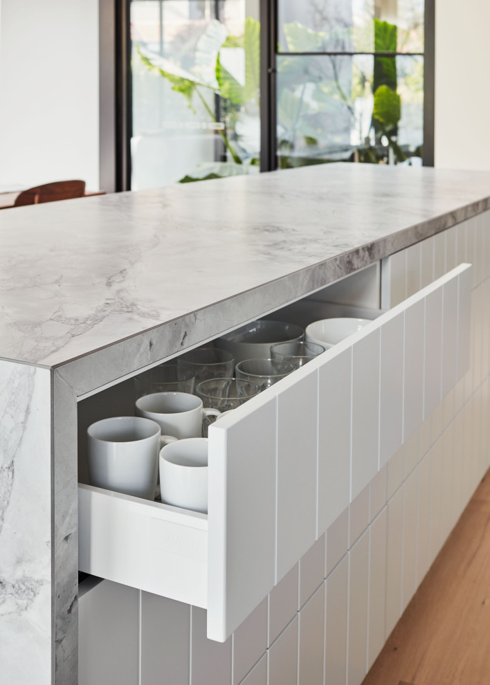Large contemporary galley eat-in kitchen in Melbourne with a drop-in sink, flat-panel cabinets, green cabinets, marble benchtops, white splashback, ceramic splashback, stainless steel appliances, light hardwood floors, with island, beige floor and white benchtop.