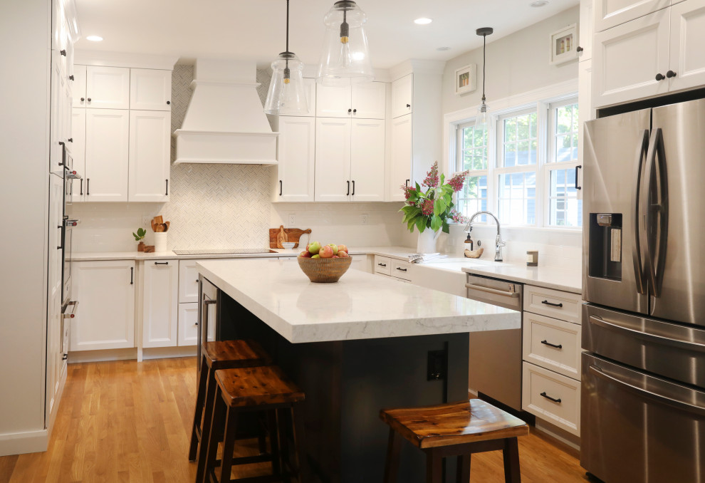 Transitional u-shaped medium tone wood floor and brown floor kitchen photo in Boston with white backsplash, a farmhouse sink, recessed-panel cabinets, white cabinets, stainless steel appliances, an island and white countertops