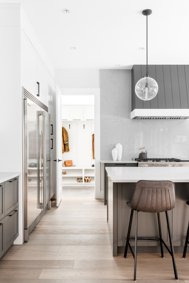 Inspiration for a large transitional l-shaped light wood floor and beige floor open concept kitchen remodel in Vancouver with shaker cabinets, gray cabinets, an island, white backsplash, glass sheet backsplash and white countertops