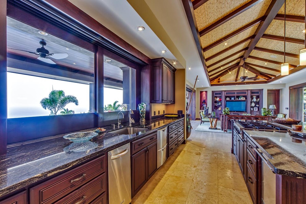 Large tropical u-shaped open plan kitchen in Hawaii with an undermount sink, raised-panel cabinets, brown cabinets, granite benchtops, black splashback, stone slab splashback, stainless steel appliances, travertine floors and with island.
