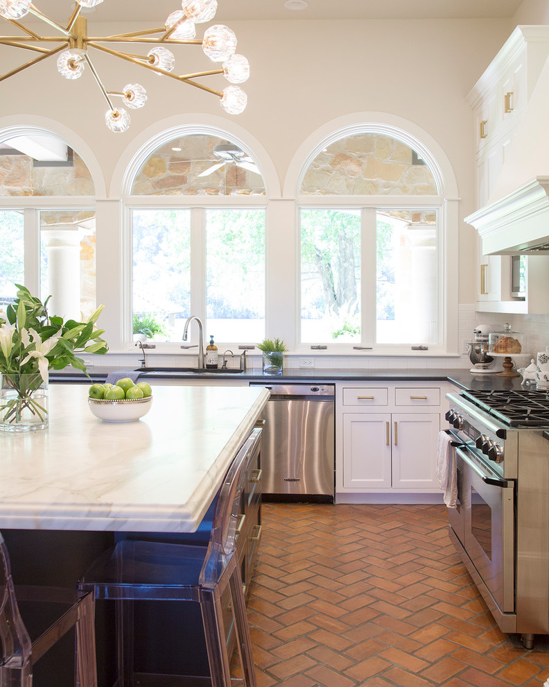 Example of a large transitional u-shaped brick floor kitchen design in Austin with an undermount sink, shaker cabinets, white cabinets, marble countertops, white backsplash, subway tile backsplash, stainless steel appliances, an island and black countertops