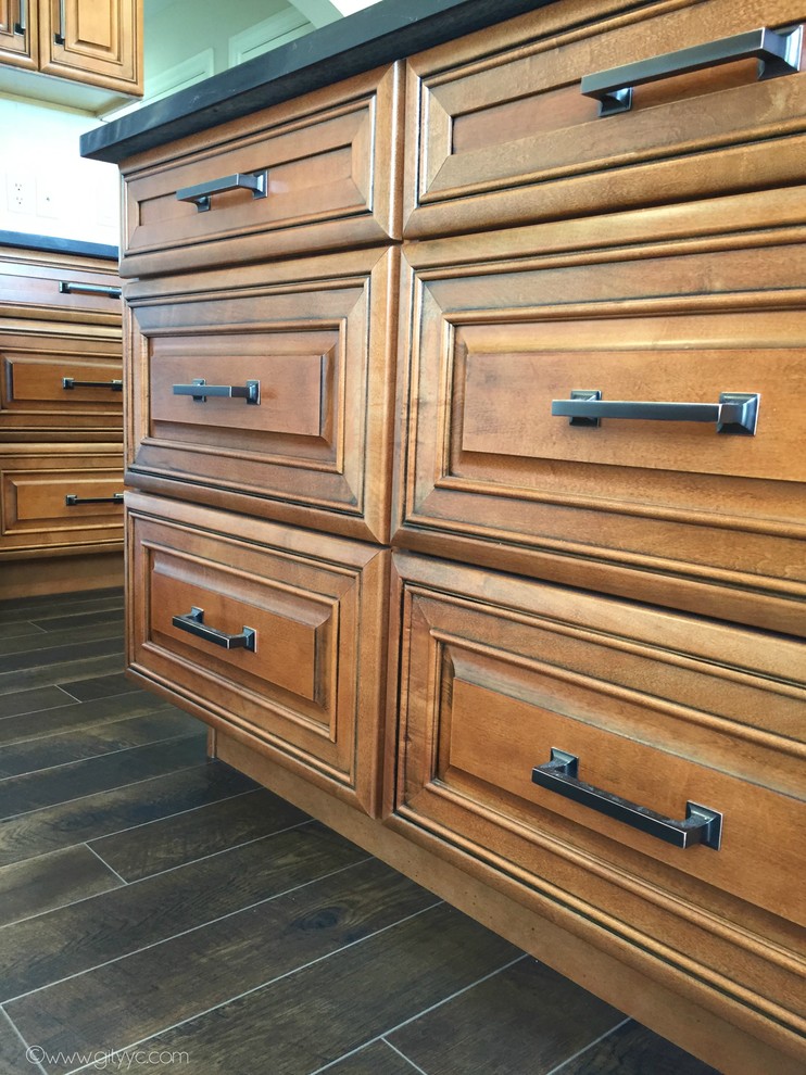 Mid-sized mountain style l-shaped laminate floor and black floor home design photo in Calgary with a drop-in sink, raised-panel cabinets, medium tone wood cabinets, quartzite countertops, white backsplash, ceramic backsplash, stainless steel appliances and an island