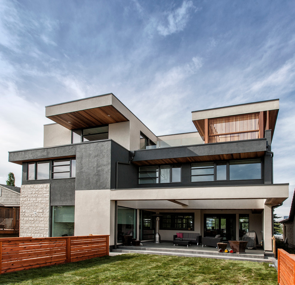 Inspiration for a large contemporary three-storey stucco beige exterior in Calgary with a flat roof.