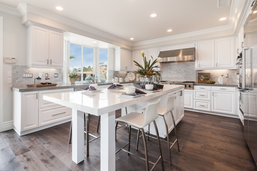Photo of a transitional u-shaped kitchen in Orange County with raised-panel cabinets, white cabinets, grey splashback, stainless steel appliances, dark hardwood floors and with island.