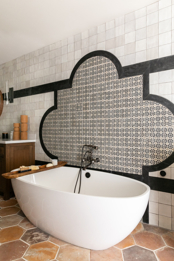 Ejemplo de cuarto de baño mediterráneo con bañera exenta, baldosas y/o azulejos blancas y negros, suelo de baldosas de terracota y suelo marrón
