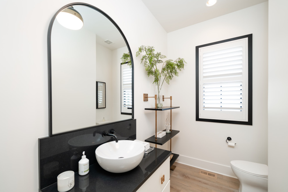 Inspiration for a contemporary powder room in Louisville with flat-panel cabinets, white cabinets, a one-piece toilet, white walls, light hardwood floors, a vessel sink, engineered quartz benchtops, brown floor, black benchtops and a built-in vanity.