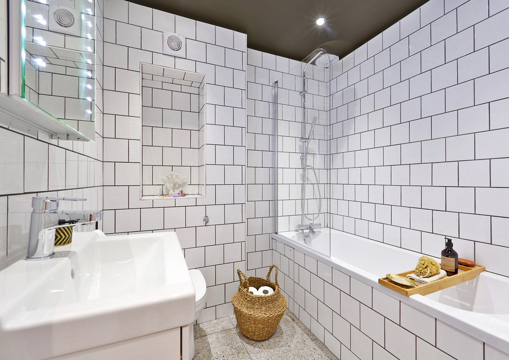 This is an example of a mid-sized contemporary kids bathroom in London with white cabinets, a shower/bathtub combo, a one-piece toilet, white tile, ceramic tile, white walls, terrazzo floors, grey floor, a hinged shower door and a corner tub.