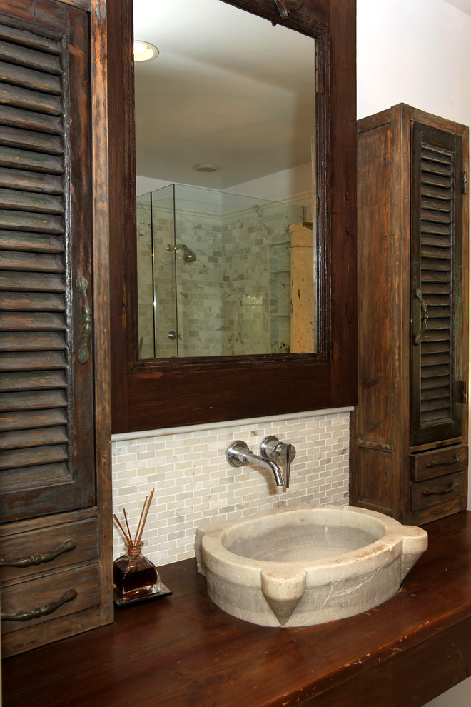 Photo of a large mediterranean bathroom in Los Angeles with distressed cabinets, wood benchtops, an undermount tub, a corner shower, a two-piece toilet, white tile, marble, grey walls, travertine floors, a vessel sink, beige floor, a hinged shower door and louvered cabinets.