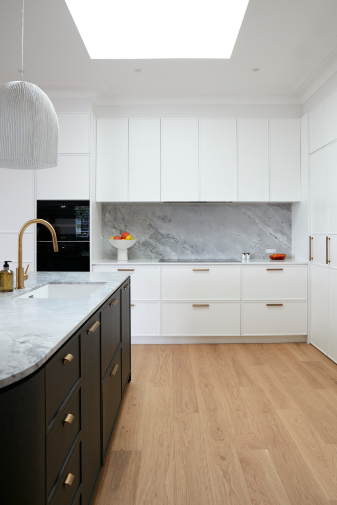 Design ideas for a mid-sized contemporary open plan kitchen in Sydney with a single-bowl sink, shaker cabinets, white cabinets, marble benchtops, white splashback, marble splashback, black appliances, light hardwood floors, with island, brown floor and white benchtop.