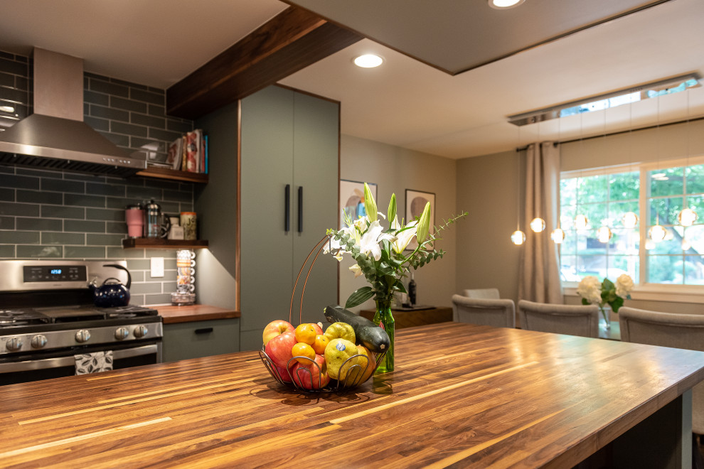 Example of a mid-sized transitional u-shaped medium tone wood floor, gray floor and exposed beam eat-in kitchen design in Denver with a farmhouse sink, flat-panel cabinets, green cabinets, wood countertops, green backsplash, glass tile backsplash, stainless steel appliances, an island and brown countertops