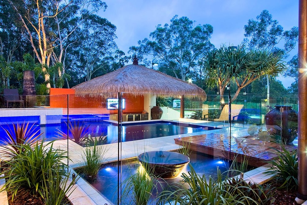 Design ideas for an expansive beach style backyard custom-shaped lap pool in Brisbane with a pool house and natural stone pavers.