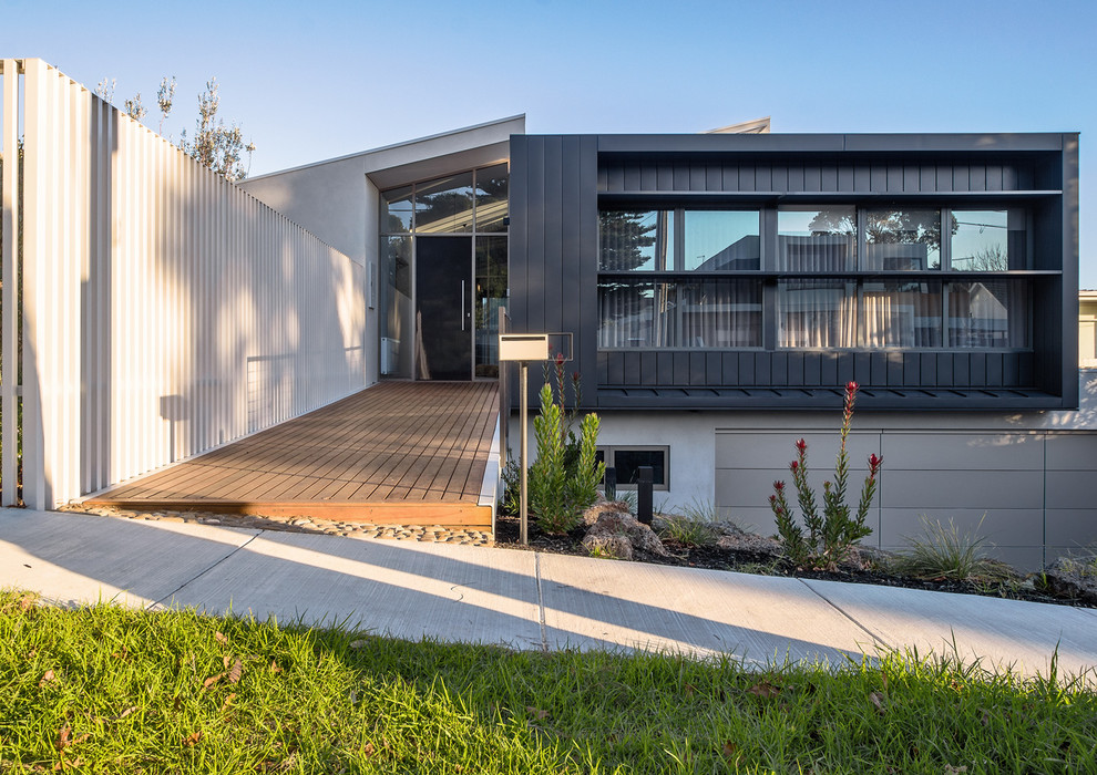 This is an example of a large modern two-storey grey house exterior in Melbourne with metal siding, a flat roof and a metal roof.