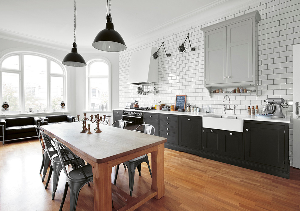 Photo of a large industrial single-wall eat-in kitchen in Copenhagen with an undermount sink, recessed-panel cabinets, black cabinets, recycled glass benchtops, black appliances, medium hardwood floors and no island.