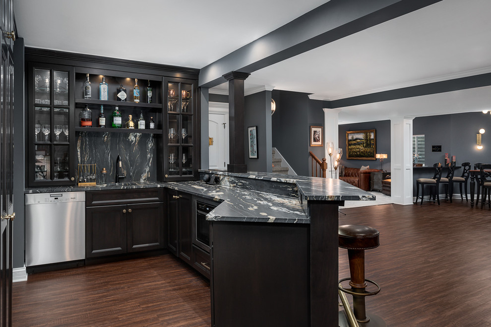 Photo of a large traditional u-shaped seated home bar in Chicago with dark hardwood floors, brown floor, an undermount sink, glass-front cabinets, black cabinets, marble benchtops, black splashback, stone slab splashback and black benchtop.