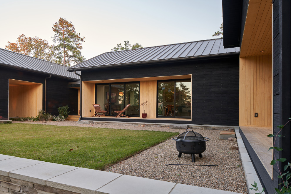 Immagine della villa nera moderna a un piano con rivestimento in pietra, tetto a capanna, copertura in metallo o lamiera, tetto grigio e pannelli sovrapposti