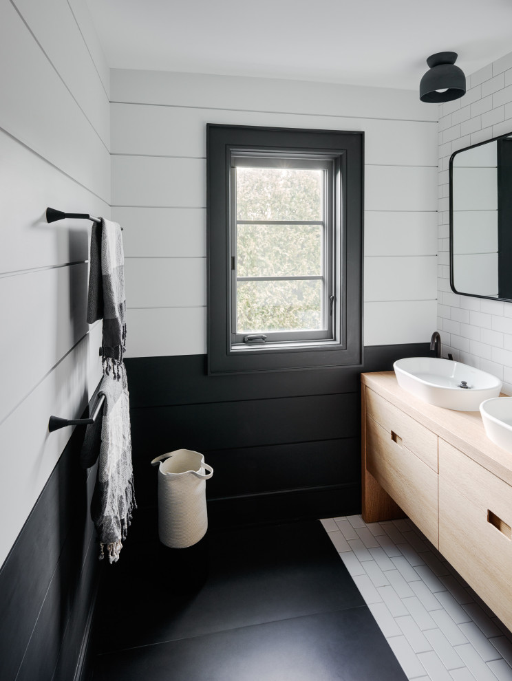 Photo of a contemporary bathroom in New York with flat-panel cabinets, light wood cabinets, white tile, subway tile, multi-coloured walls, a vessel sink, wood benchtops and black floor.