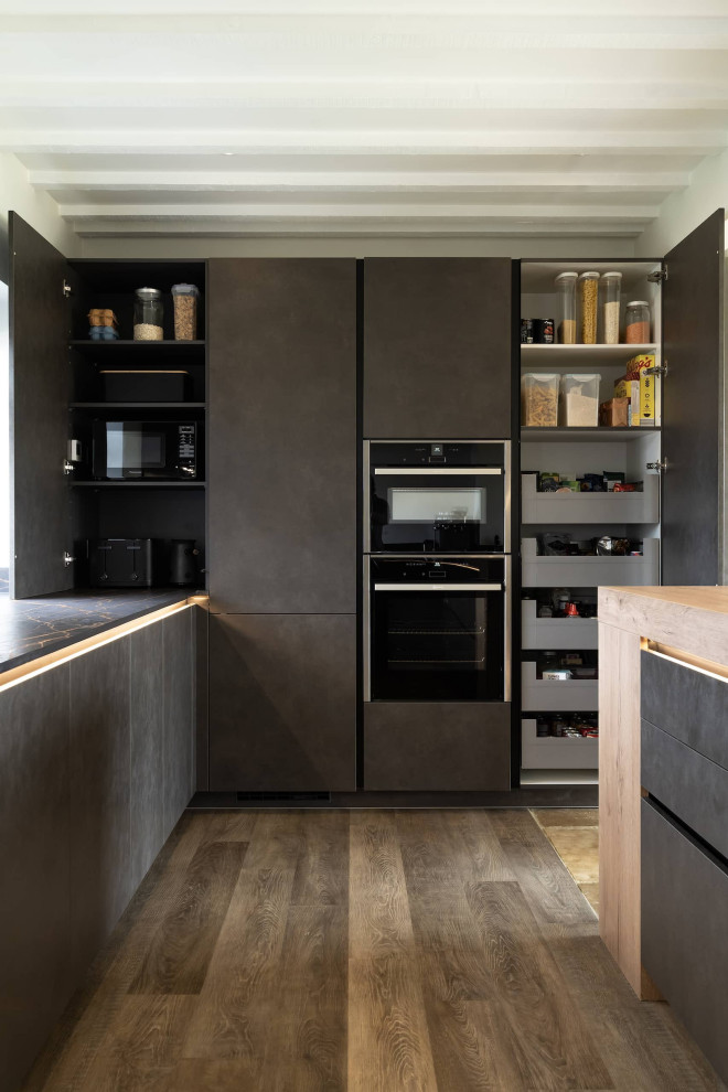 Design ideas for a large modern l-shaped open plan kitchen in Oxfordshire with flat-panel cabinets, black cabinets, quartzite benchtops, brown splashback, black appliances, a peninsula and black benchtop.