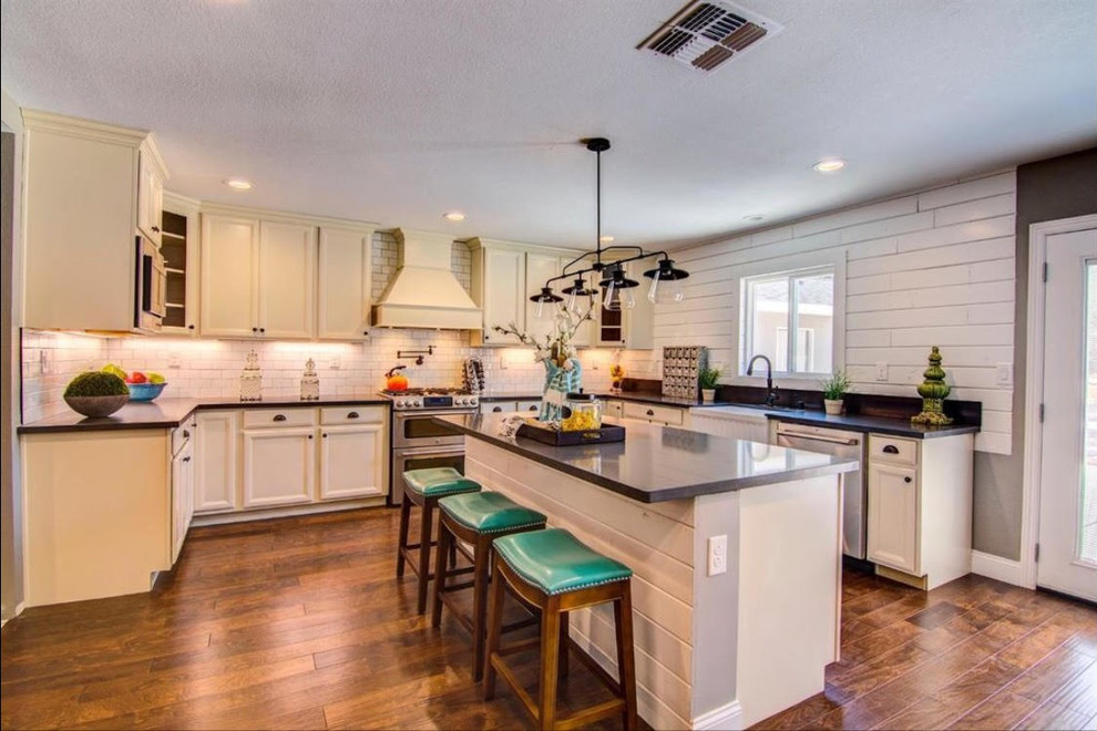 This is an example of a large country u-shaped open plan kitchen in Sacramento with a farmhouse sink, recessed-panel cabinets, white cabinets, white splashback, subway tile splashback, stainless steel appliances, medium hardwood floors, with island and brown floor.