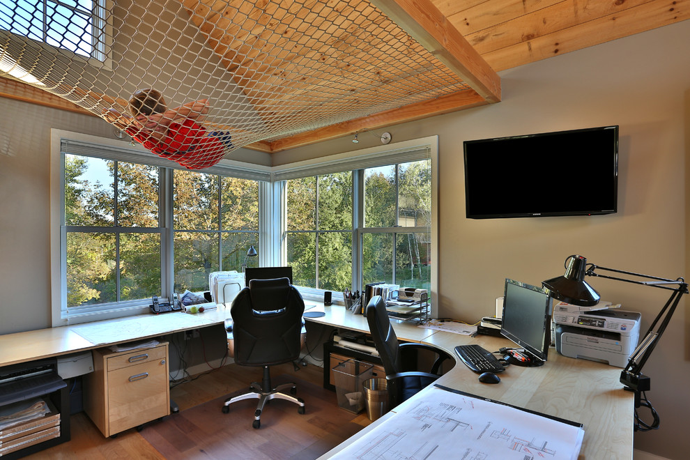 Transitional home studio in Portland Maine with medium hardwood floors, a built-in desk, brown floor and grey walls.
