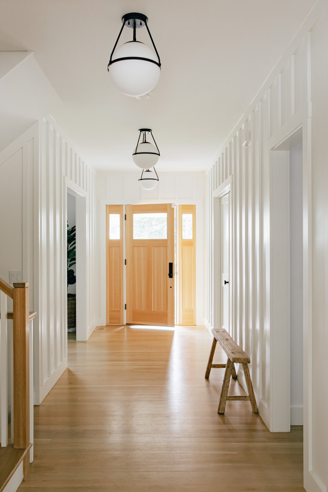 Idee per un grande ingresso stile marino con pareti bianche, parquet chiaro, una porta singola, una porta in legno chiaro, pavimento marrone e pannellatura