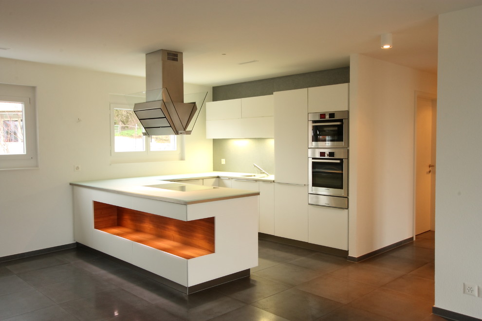 This is an example of a mid-sized modern u-shaped open plan kitchen in Essen with a peninsula, glass-front cabinets, white cabinets, glass benchtops, white splashback, stainless steel appliances, an undermount sink and ceramic floors.