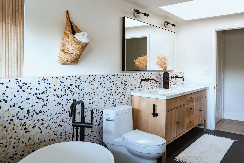Design ideas for a contemporary ensuite bathroom in Orange County with flat-panel cabinets, medium wood cabinets, a freestanding bath, a one-piece toilet, white walls, a submerged sink, marble worktops, black floors, white worktops, double sinks and a built in vanity unit.
