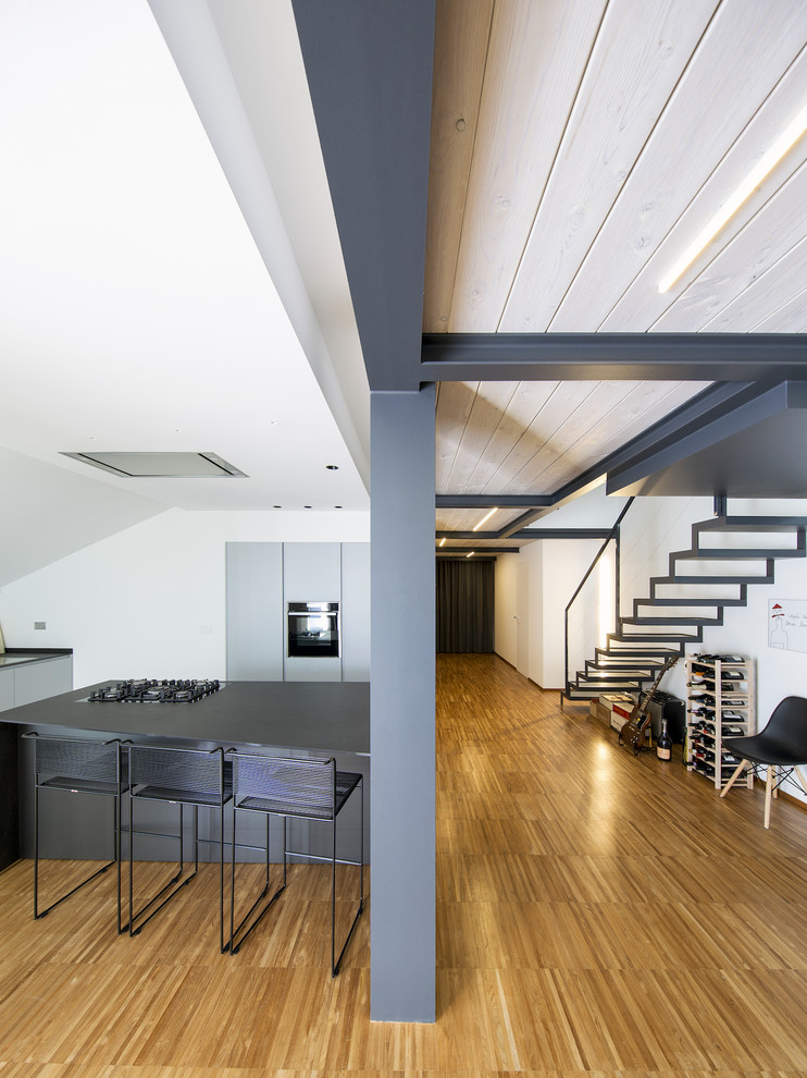 Contemporary kitchen in Turin with flat-panel cabinets, grey cabinets, black appliances, bamboo floors, with island and grey benchtop.