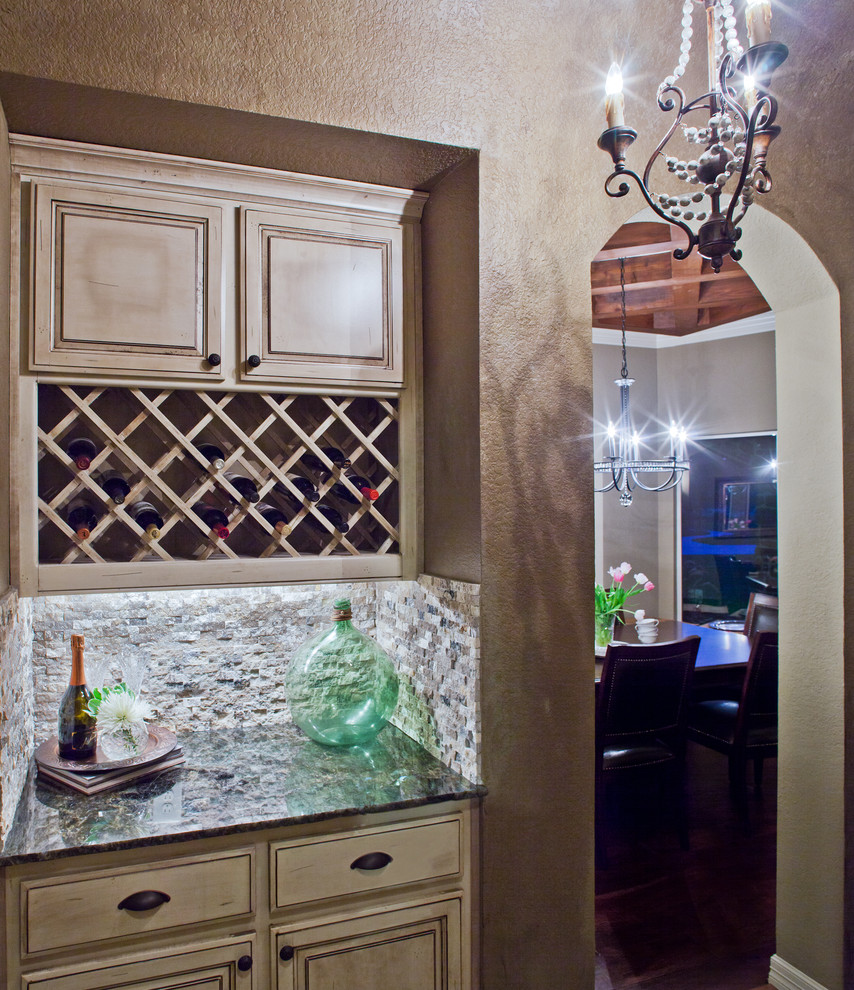 This is an example of a mid-sized traditional galley home bar in Houston with raised-panel cabinets, distressed cabinets, granite benchtops, beige splashback, stone tile splashback and travertine floors.