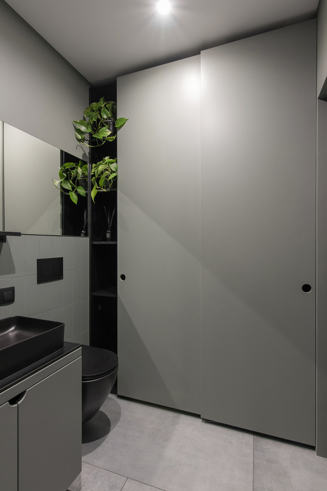 Cette image montre un petit WC et toilettes design avec des portes de placards vertess, un carrelage vert, un mur vert, un sol gris, un plan de toilette noir et meuble-lavabo sur pied.