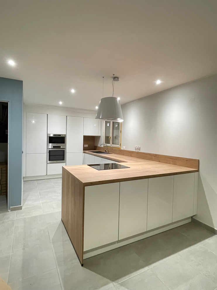 This is an example of a large scandi u-shaped open plan kitchen with a submerged sink, all styles of cabinet, white cabinets, wood worktops, wood splashback, integrated appliances, ceramic flooring, a breakfast bar and grey floors.