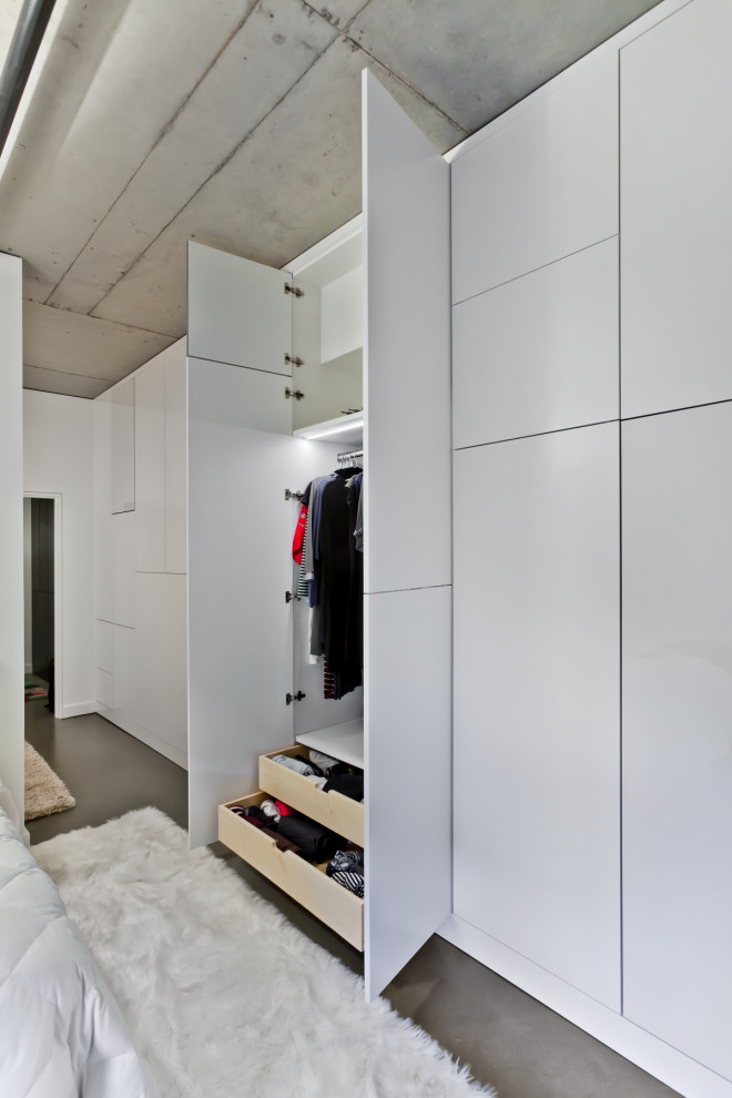 This is an example of a large gender-neutral built-in wardrobe in Minneapolis with concrete floors, flat-panel cabinets and white cabinets.