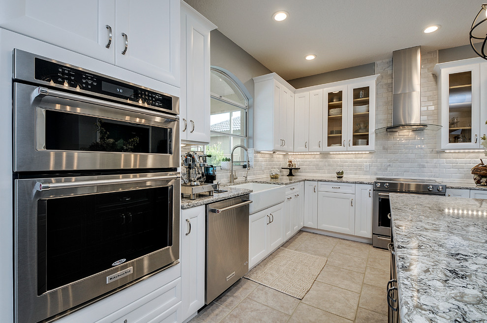 Example of a transitional ceramic tile kitchen design in Tampa with a farmhouse sink, white cabinets, white backsplash, stone tile backsplash, stainless steel appliances and an island