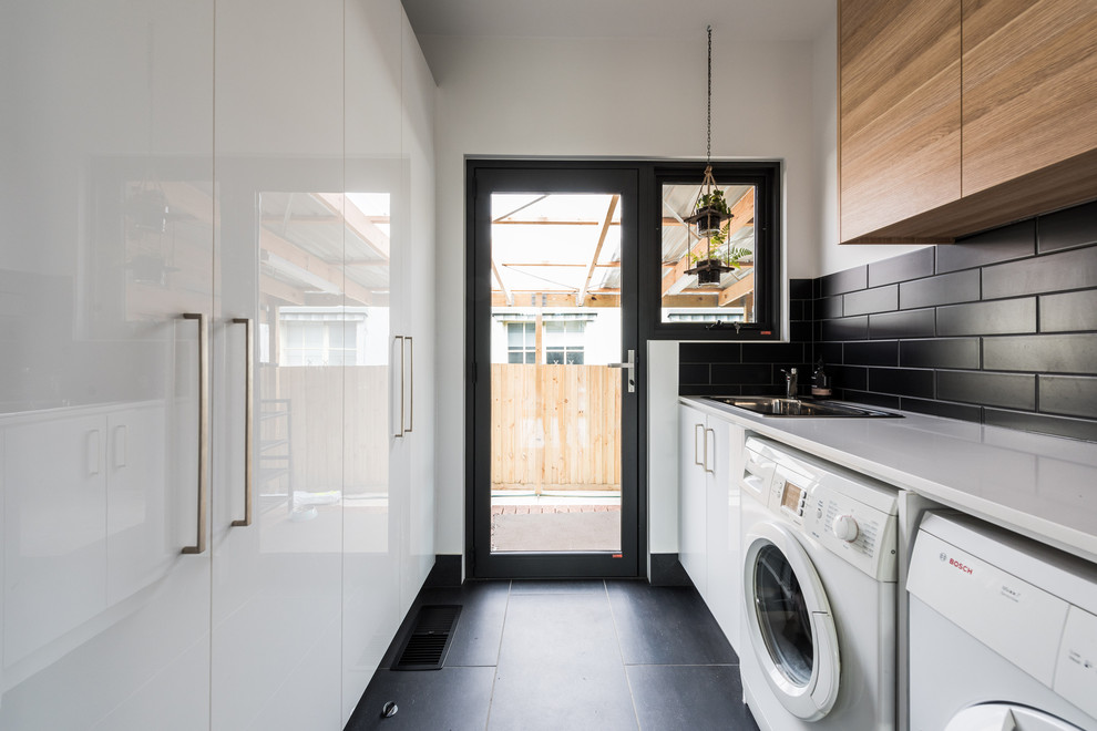 Photo of a mid-sized contemporary galley dedicated laundry room in Melbourne with a single-bowl sink, flat-panel cabinets, light wood cabinets, quartz benchtops, white walls, porcelain floors, a side-by-side washer and dryer, grey floor and white benchtop.