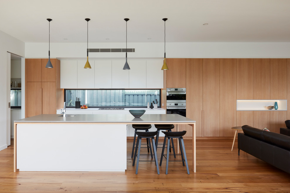 Design ideas for a mid-sized contemporary galley open plan kitchen in Adelaide with an undermount sink, beaded inset cabinets, light wood cabinets, concrete benchtops, panelled appliances, medium hardwood floors, with island, brown floor, grey benchtop and window splashback.