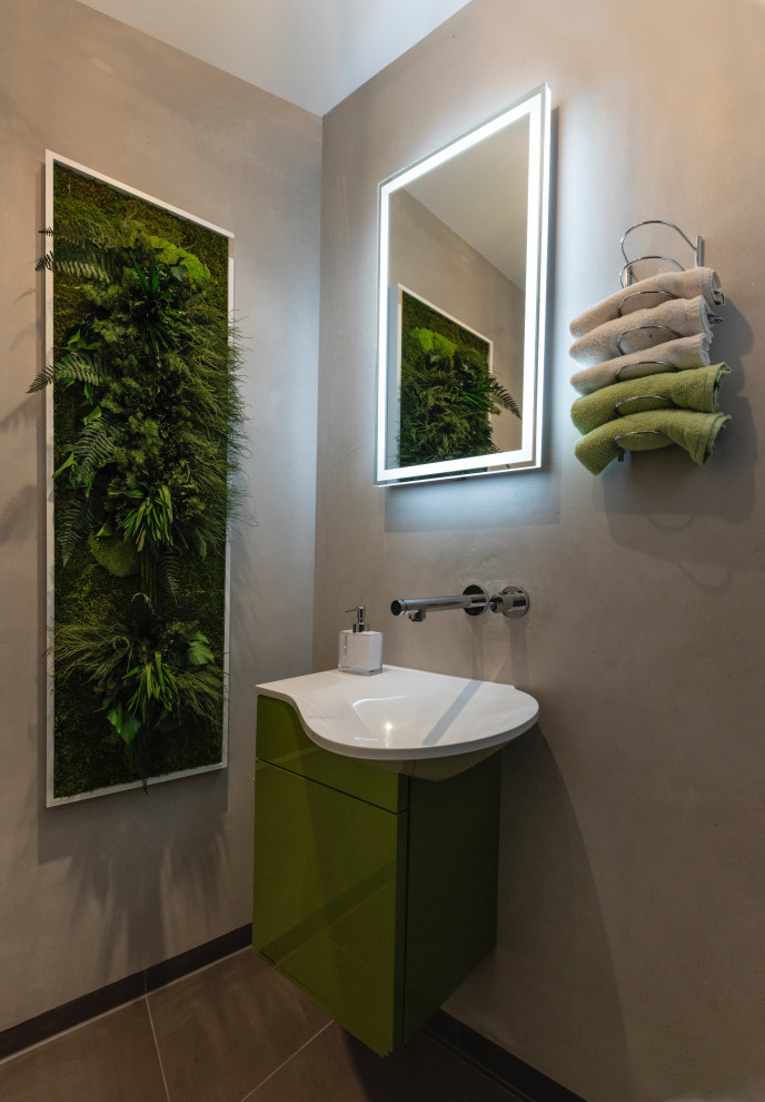 Photo of a small contemporary cloakroom in Munich with flat-panel cabinets, green cabinets, a wall mounted toilet, beige walls, solid surface worktops, grey floors, white worktops, a built in vanity unit and an integrated sink.